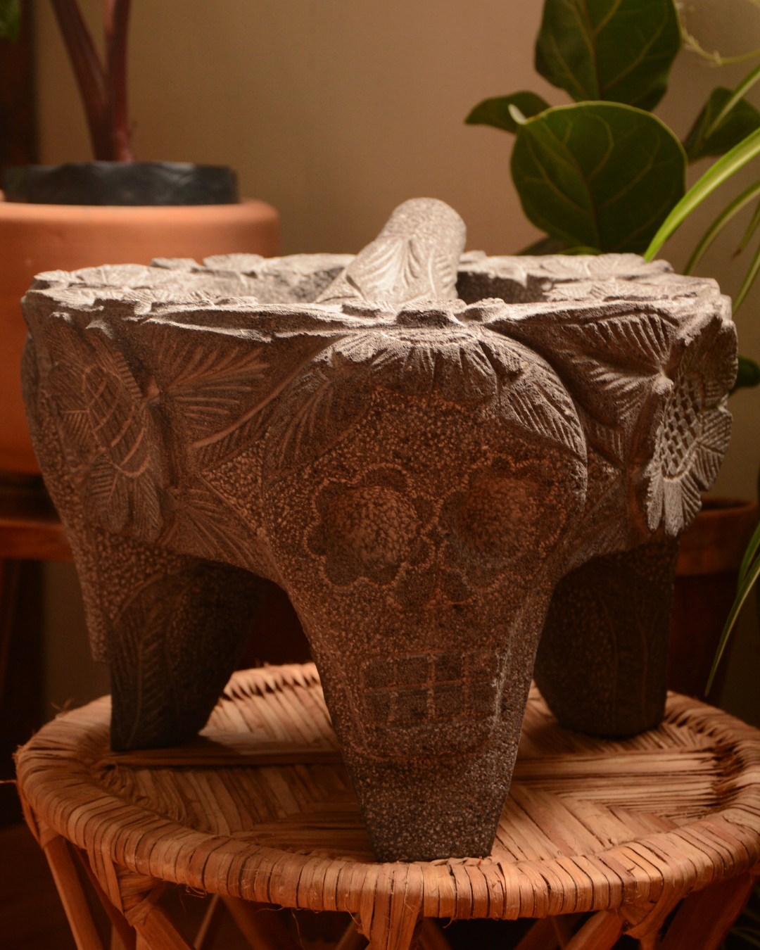 Molcajete labrado de piedra volcánica con calaveras y flores.